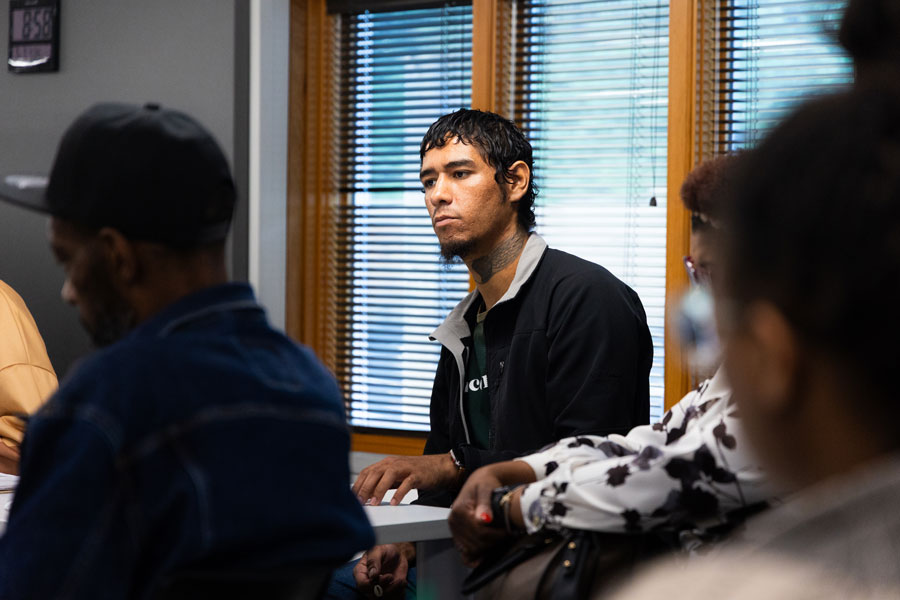 A man in focus sitting in a room full of other people that are slightly blurred