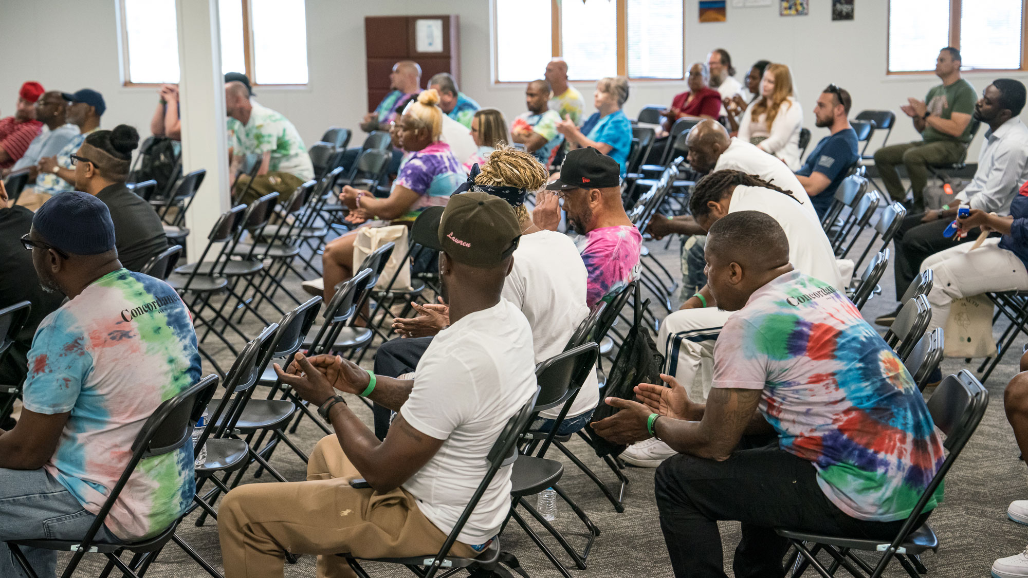 A large group of people sit in folding chairs all facing the front of a room.